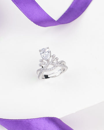 The Vintage Romance CZ Ring in Demifine Sterling Silver by Chandrani Pearls, featuring a pear-shaped clear CZ and delicate details, is showcased on a white surface with purple ribbon accents.