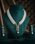 The Saratas - Mystic Mints Pearl Necklace Set by Chandrani Pearls, featuring a multi-strand design with pearls and emeralds, complete with matching earrings, is beautifully displayed on a dark green stand.