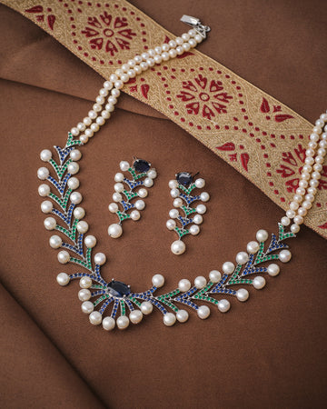 The Luxe Pearl Beautiful Necklace Set by Chandrani Pearls with matching earrings is displayed on brown fabric beside a gold and red embroidered textile.