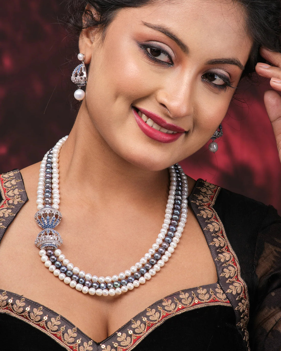 Chandrani Pearls' Side Pendant Necklace—Subtle Elegance with a Modern Twist—paired with blue-accented jhumka earrings, radiates style and sophistication on a pink surface next to folded purple fabric.