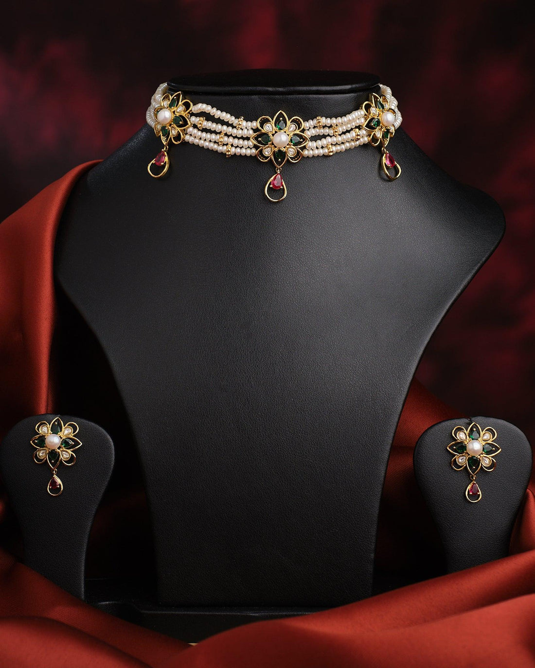 The Ethnic Blooming Necklace Set by Chandrani Pearls India features a pearl and gold floral choker with matching earrings, elegantly displayed on black against a red and black background—ideal for formal occasions and elegant gatherings.