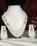A white display stand features the Flory Double Side Necklace Set by Chandrani Pearls India—a sophisticated three-layer pearl necklace with gold and stone accents, paired with matching pearl drop earrings.
