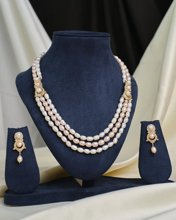 The Chandrani Pearls Layered CZ Necklace & Earring Set is showcased on navy blue velvet stands, creating an elegant and dramatic effect against a draped fabric background.