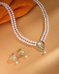 The Celina CZ Pearl Set by Chandrani Pearls—featuring a refined double-strand pearl necklace with a gold and gemstone pendant plus matching pearl and gold earrings—radiates timeless brilliance on a tan background.