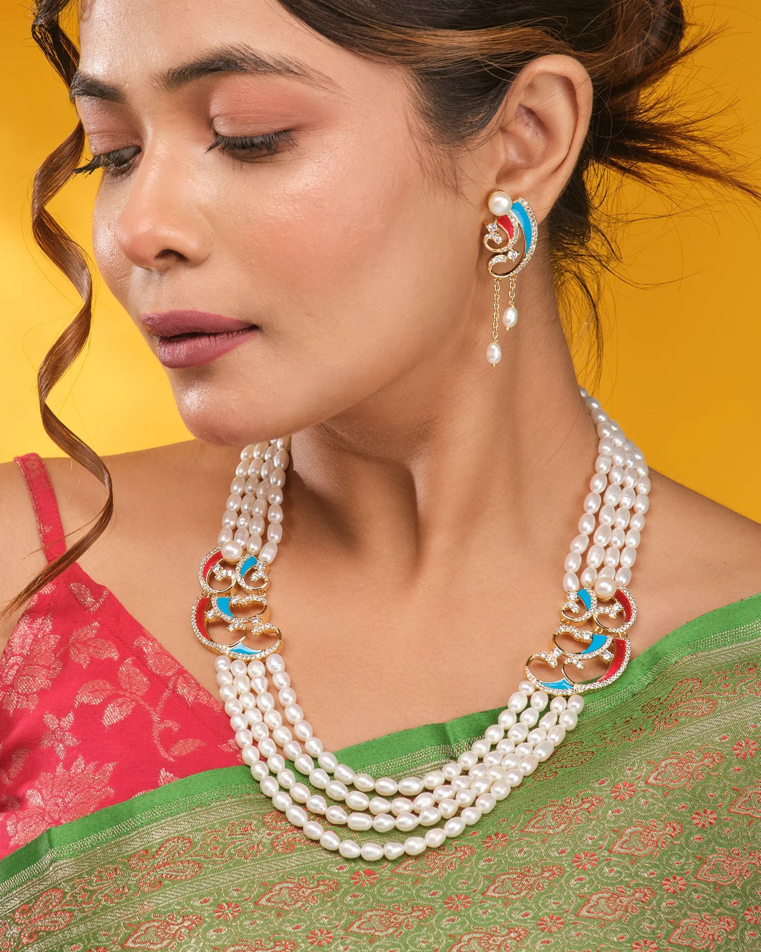The Graceful Queen Pearl CZ Necklace Set by Chandrani Pearls features three strands with gold, red, and blue accents, plus matching earrings, displayed on brown fabric with a patterned border—exuding regal grace.