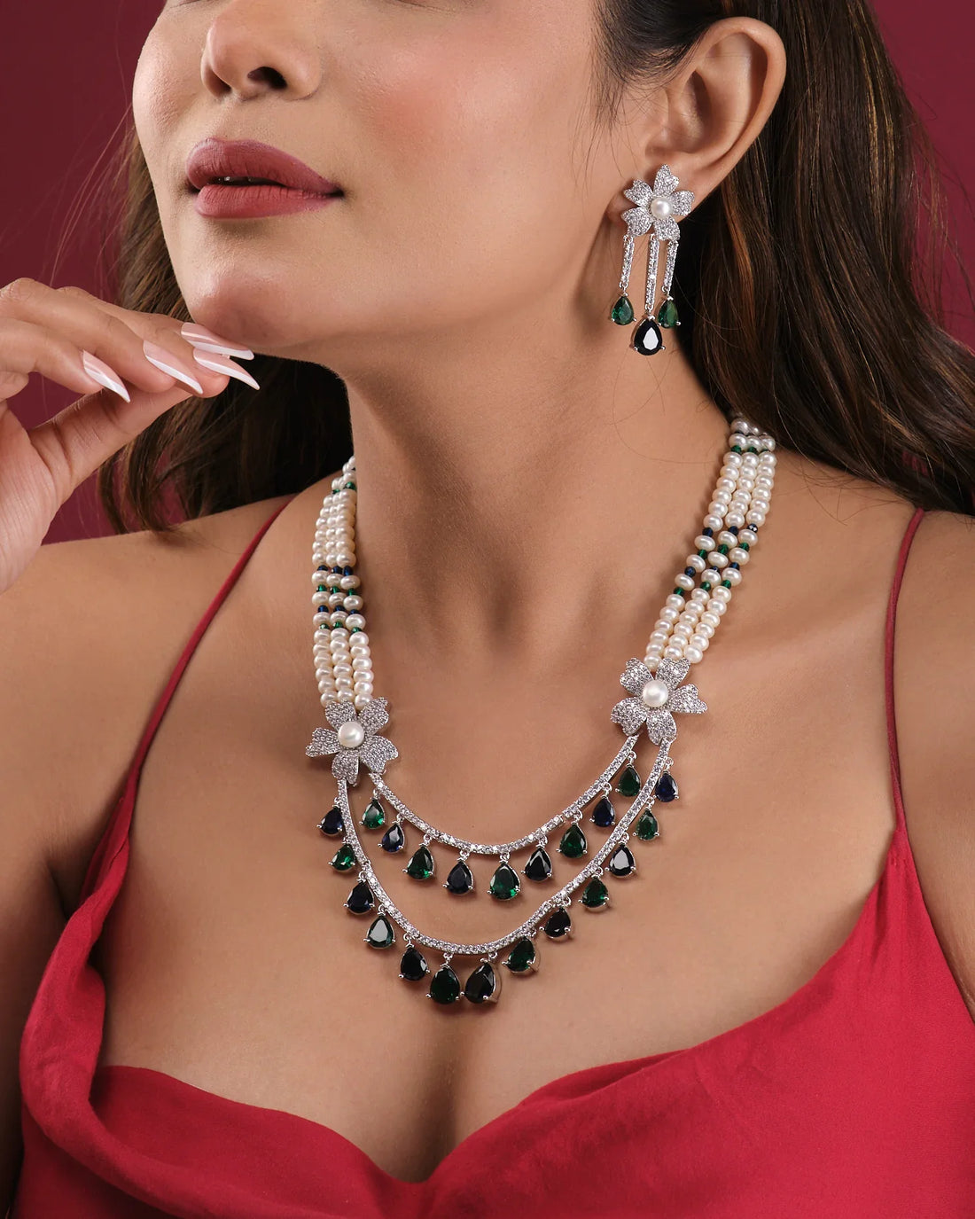 The Beautiful Ravishing Pearl Necklace Set by Chandrani Pearls India, featuring pearls, diamonds, and emeralds with matching earrings, is showcased on a white jewelry stand against a neutral background.