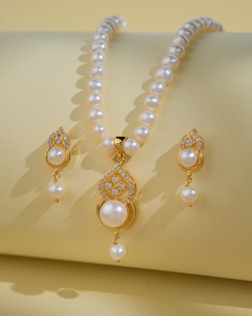 The Pretty Pearl Necklace Sets by Chandrani Pearls India, featuring a necklace and matching earrings with luminous pearls and clear stones, are displayed on a pale yellow background to accentuate their elegance.