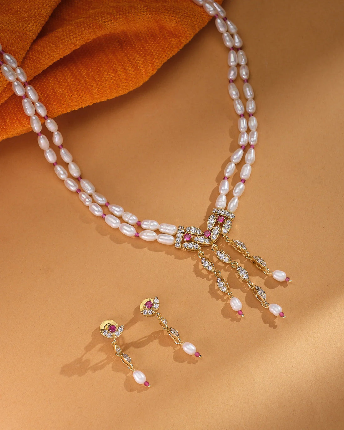 The Chandrani Pearls Vintage-Inspired Beads & Pearl & Crystal Set adds Hollywood charm with three dangling pendants and matching drop earrings, displayed elegantly on a beige surface.