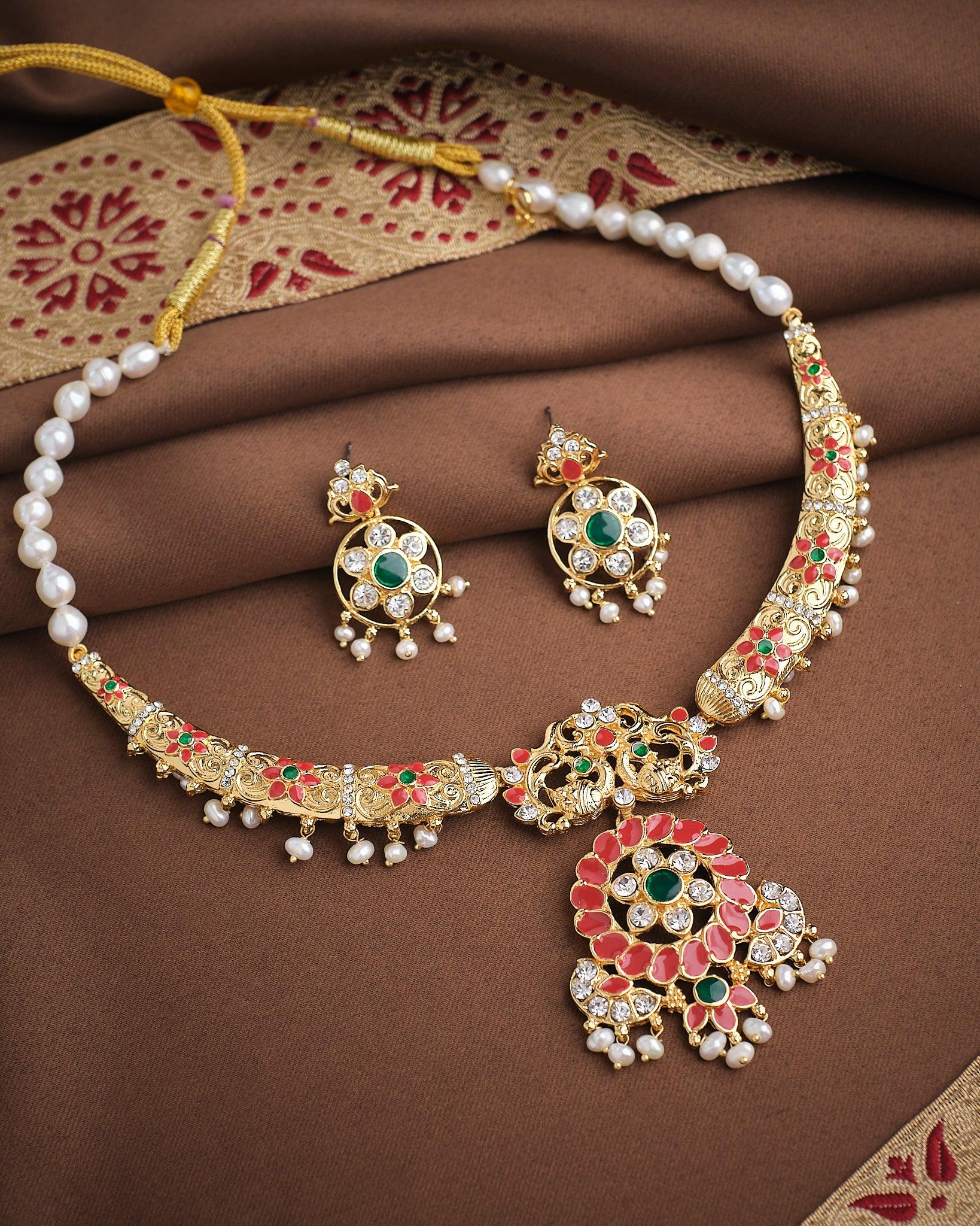 The Imperial Enamel Halo Pearl CZ Set by Chandrani Pearls features a gold and pearl necklace with matching earrings, adorned with green, red, and white enamel accents and haloed pearls, displayed on brown and gold patterned fabric.