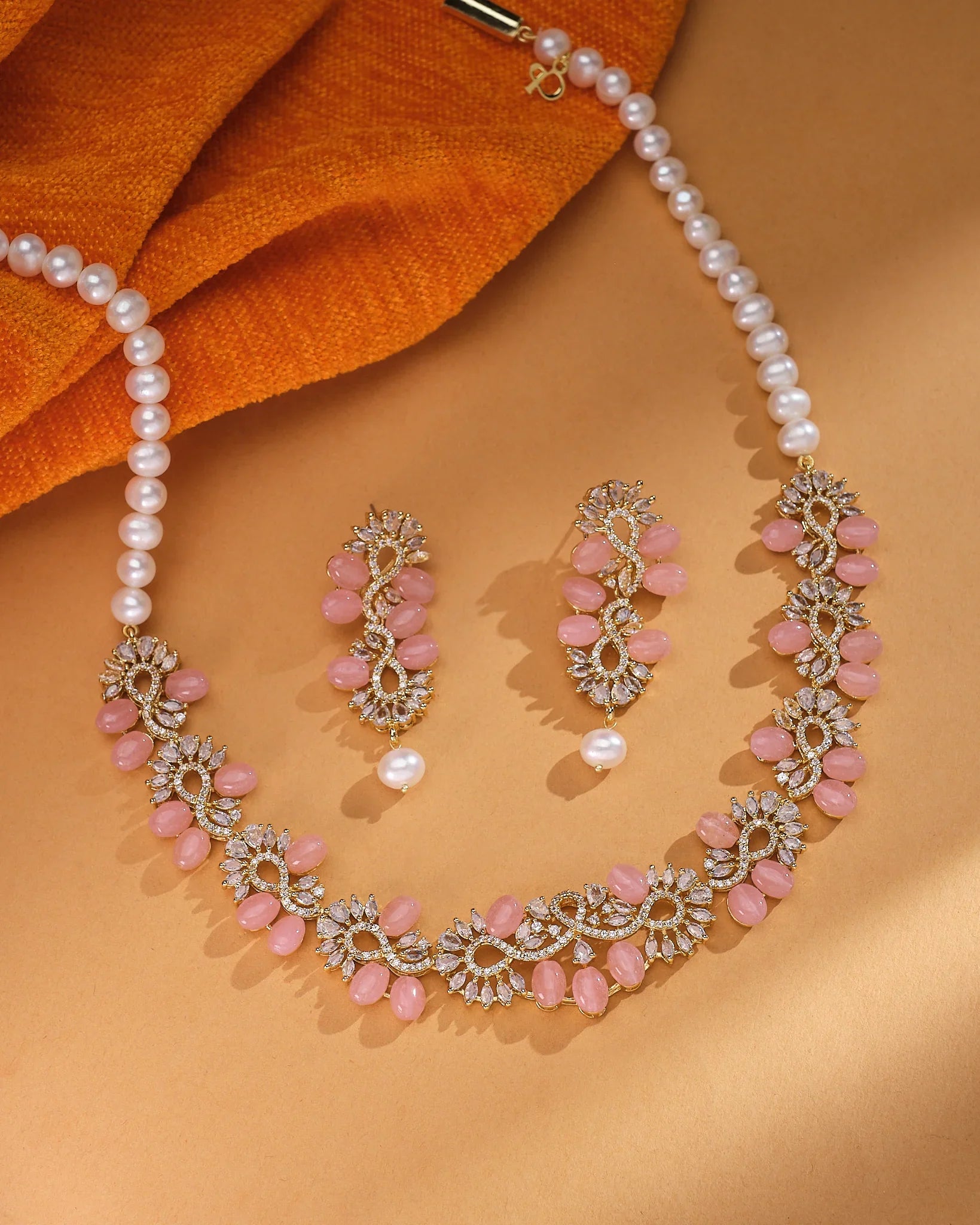 The Chandrani Pearls Petite Pink CZ Pearl Necklace Set Delicate Beauty, shown with matching earrings on beige and orange fabric, is ideal for lovers of elegant minimalist jewelry.