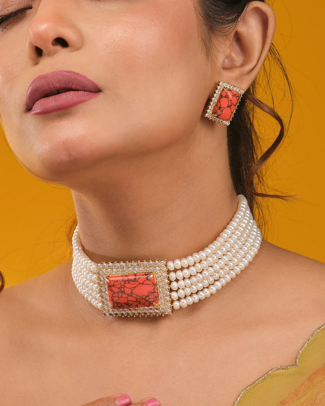 The Trendsetter Pearl Necklace Choker & Earrings by Chandrani Pearls features a bold rectangular orange stone pendant and matching earrings, elegantly presented on a tan surface with orange fabric in the background.