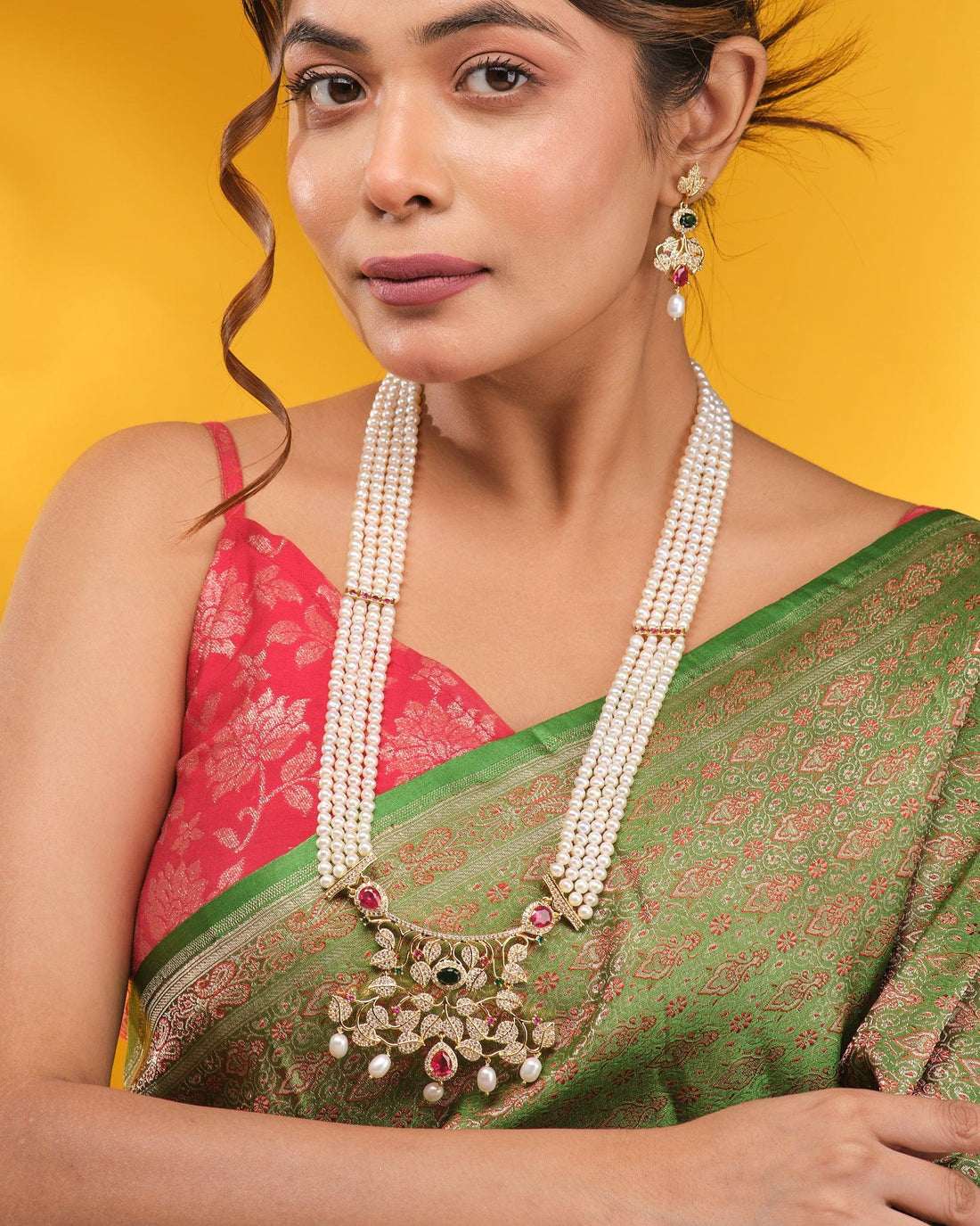 The Noor Floral Supreme Pearl CZ Sita Set by Chandrani Pearls features premium pearls, a gold and gemstone pendant with high-grade CZ stones, and matching earrings, beautifully displayed on brown fabric with a decorative border.