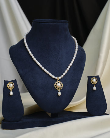 The Dazzling Floral CZ Necklace Set by Chandrani Pearls, featuring a pearl pendant, is showcased on a dark blue stand with matching gold and pearl drop earrings.