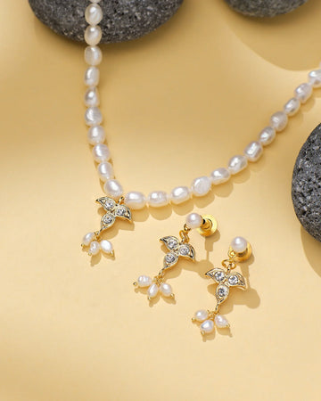 The Pearl Radiance CZ Necklace Set by Chandrani Pearls includes a radiant pendant and matching gold earrings with pearl and crystal details, beautifully arranged on a light yellow surface with black stones.