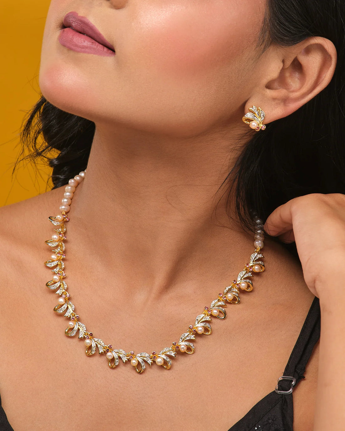 The Twilight Pearl Radiance Set by Chandrani Pearls—a gold and natural pearls necklace with matching stud earrings—is displayed on a tan surface beside orange fabric, perfect for occasion wear.