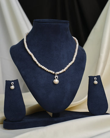 The Chandrani Pearls CZ Halo Pendant Set features a pearl necklace with matching pendant and earrings, each accented by CZ stone halos, elegantly displayed on navy blue velvet against a cream and black fabric background.