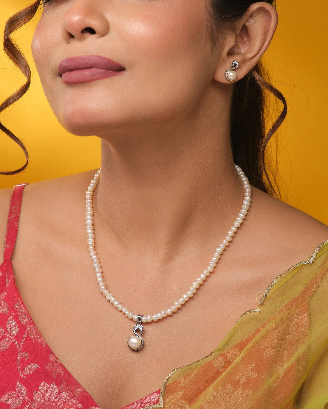 The Chandrani Pearls CZ Halo Pendant Set features a pearl necklace with matching pendant and earrings, each accented by CZ stone halos, elegantly displayed on navy blue velvet against a cream and black fabric background.