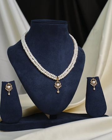 The Elegant round-cut CZ pendant with matching earrings by Chandrani Pearls, displayed on a navy stand, offers timeless style—designed to add everyday sparkle to your look.