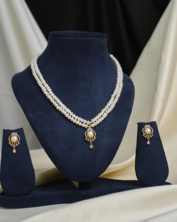 The Chandrani Pearls Sparkling Halo CZ necklace is displayed on a navy blue stand, paired with matching stud earrings on either side, all radiating a luxurious shine.