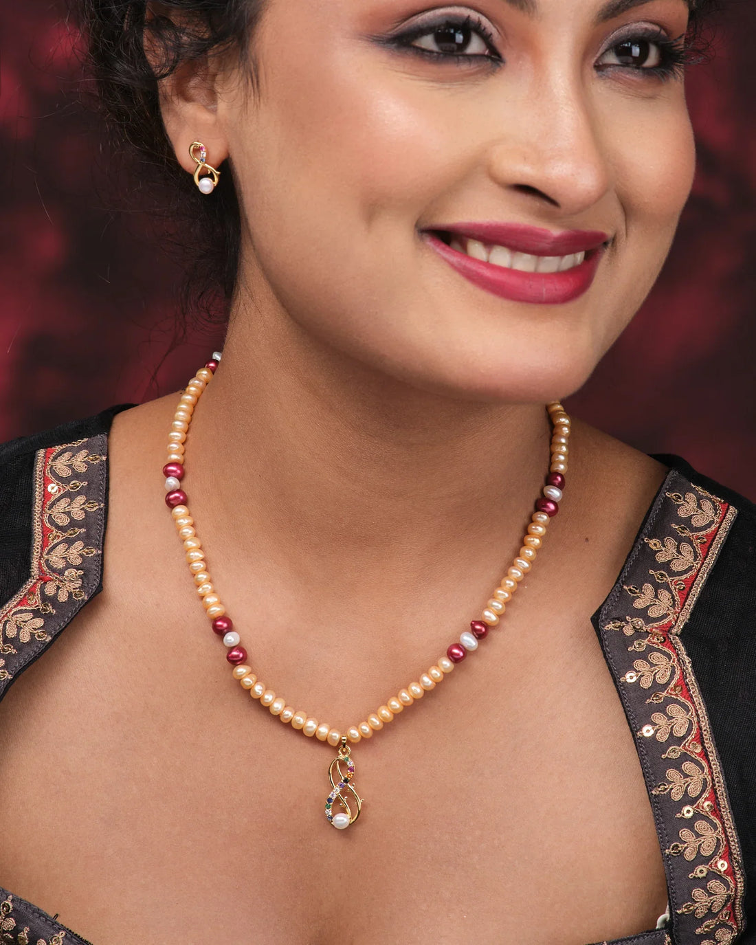 The Elegant Pearl Necklace Set by Chandrani Pearls features a pearl and gold bead necklace with a matching pendant and earrings, displayed on pink with a folded purple cloth, offering subtle design for maximum shine.