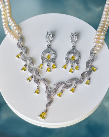 The Vintage-Inspired Bridal Pearl Set by Chandrani Pearls features a pearl necklace with a diamond and yellow gemstone pendant, CZ accents, and matching drop earrings—ideal for commemorating unforgettable moments.