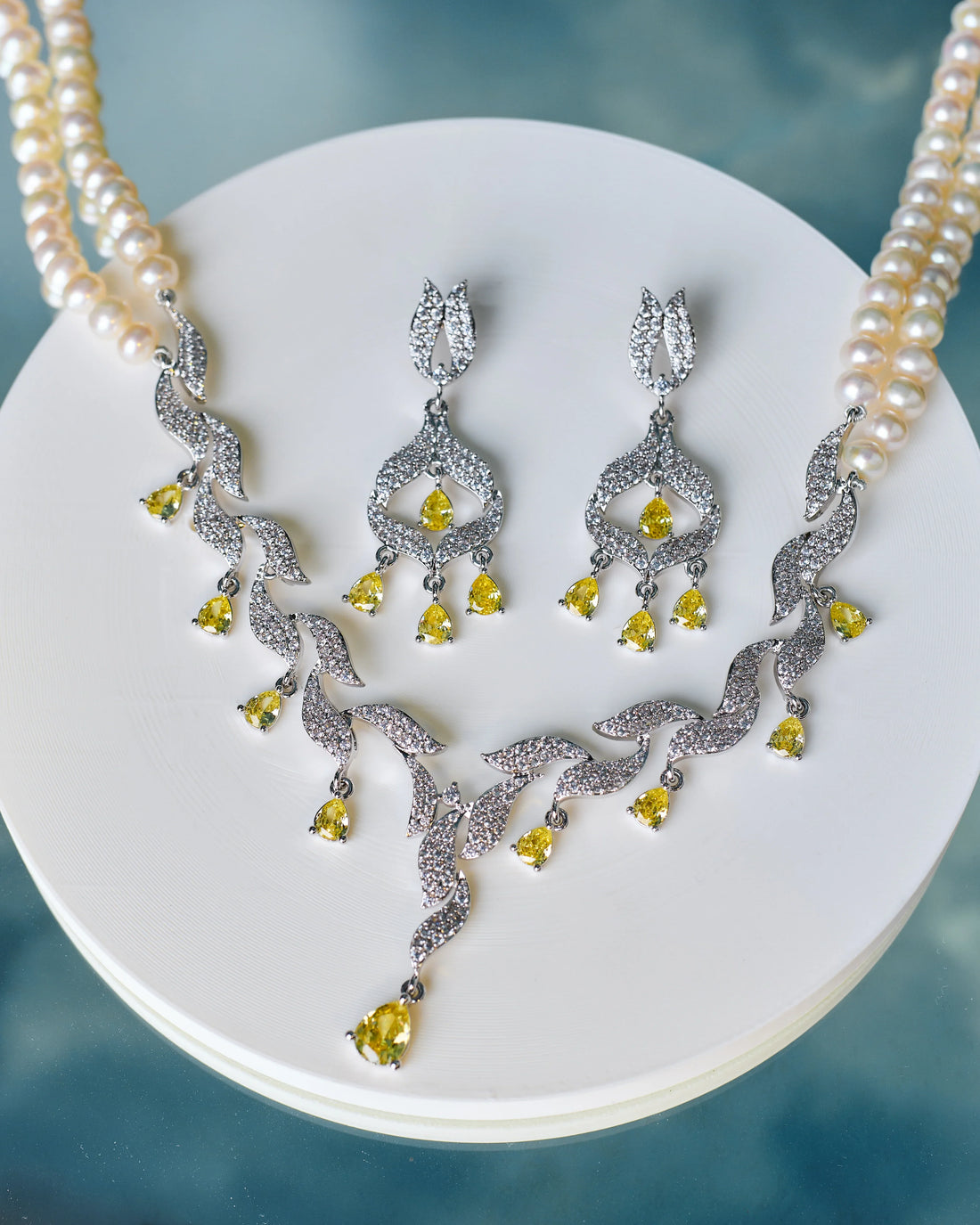 The Vintage-Inspired Bridal Pearl Set by Chandrani Pearls features a pearl necklace with a diamond and yellow gemstone pendant, CZ accents, and matching drop earrings—ideal for commemorating unforgettable moments.