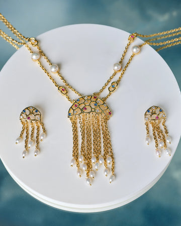 The Trendy Handcrafted Chain & CZ Necklace Set by Chandrani Pearls features colorful gemstones, CZ stones, and pearls in a multi-chain design with matching earrings, elegantly displayed on a white circular stand.