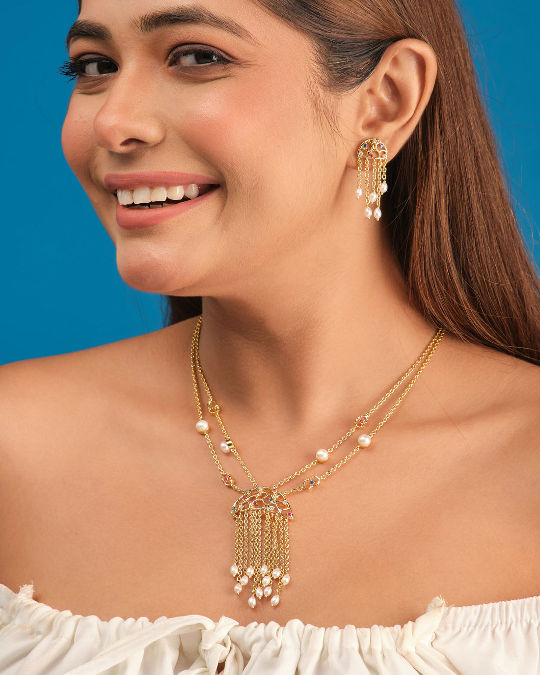 The Trendy Handcrafted Chain & CZ Necklace Set by Chandrani Pearls features colorful gemstones, CZ stones, and pearls in a multi-chain design with matching earrings, elegantly displayed on a white circular stand.