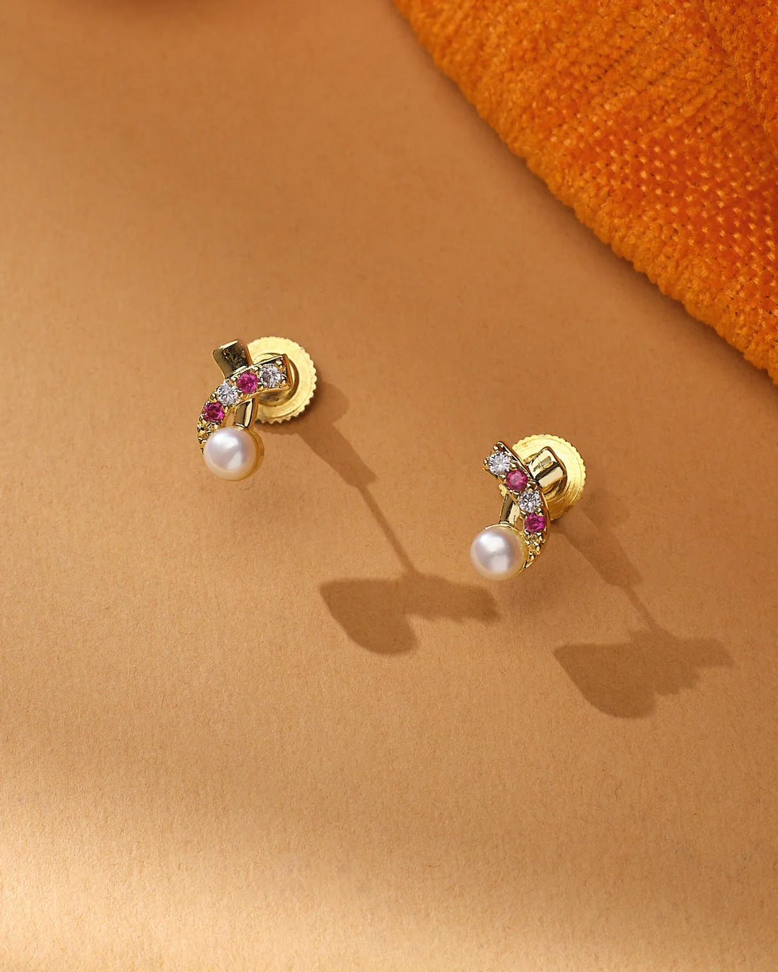 The Elegant Bloom CZ Pearl Earrings by Chandrani Pearls feature gold cross flower studs with pink stones, CZ accents, and a round white pearl on each, displayed on a neutral surface.