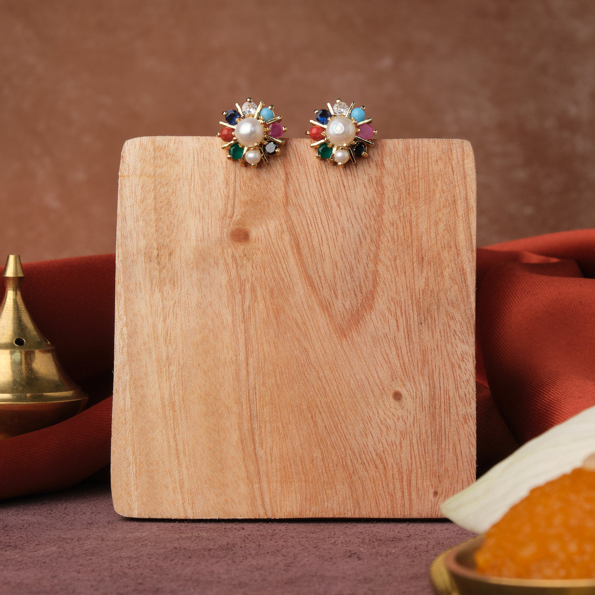 A wooden block with Chandrani Pearls India's Navratan CZ Stud Earring on it.