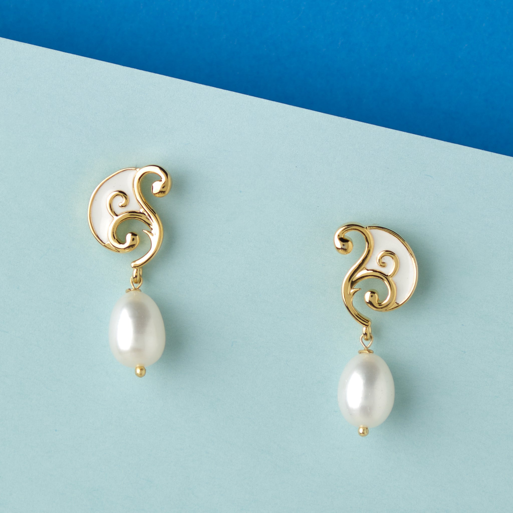 A pair of Chandrani Pearls Sophisticated Dainty Pearl Drop Earrings on a blue background.