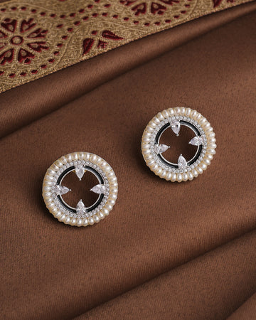 The Noor Moonlit Mirage Studs by Chandrani Pearls feature round pearls with a delicate silver border, elegantly displayed on brown fabric—perfect for any occasion.