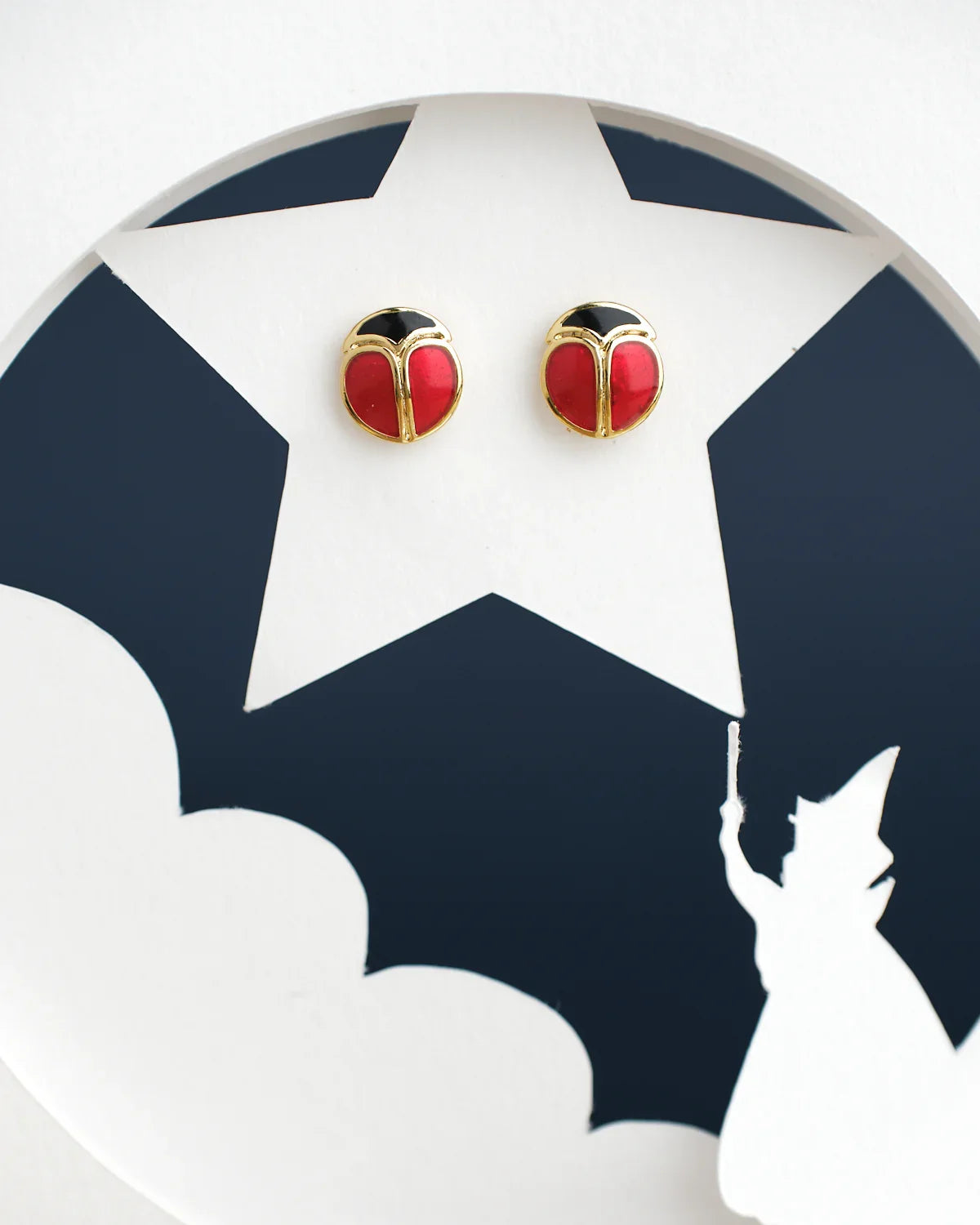 Chandrani Pearls India's Cute Stud Earrings feature a red and black round design on a white star-shaped cutout, complete with a casting figure silhouette at the bottom.