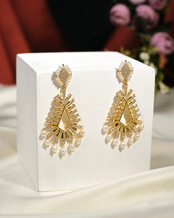 Define your Victory Hang Jhumki by Chandrani Pearls India: gold-toned geometric chandelier earrings with sparkling stones and pearl-like drops, elegantly displayed on a white cube—ideal for elevating any outfit.