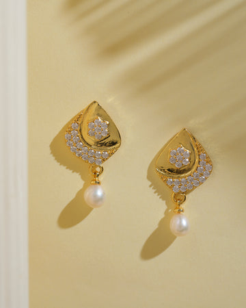 Fashionable Hanging Pearl Earrings by Chandrani Pearls India feature gold accents, small white crystals, and a radiant pearl on each earring, elegantly displayed against a pale yellow background.