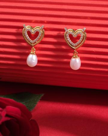 Hearty Bliss 925 Silver Earrings by Chandrani Pearls India—heart-shaped with small diamonds and dangling pearls—add sophistication, elegantly displayed on a red background with a rose in the foreground.