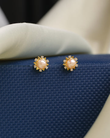 Delicate pearls suspended beneath radiant CZ studs by Chandrani Pearls are elegant gold earrings featuring central pearls and sparkling CZ accents, presented on a textured blue surface for a sophisticated look.
