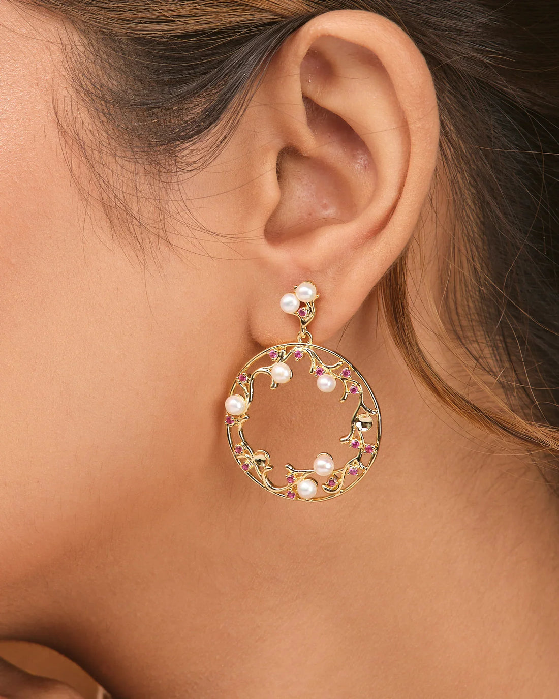 Golden Glam Pearl Earrings by Chandrani Pearls, featuring pearls, pink stones, and delicate CZ accents, displayed on a beige surface with orange fabric partially visible.