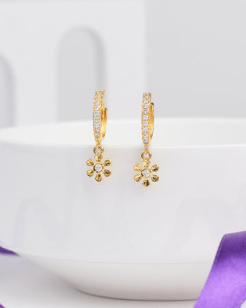 Glow Mood Silver Earrings by Chandrani Pearls feature flower-shaped pendants with stone-accented petals, adding a mood-lifting touch to your laid-back style and elegantly displayed over the rim of a white bowl.