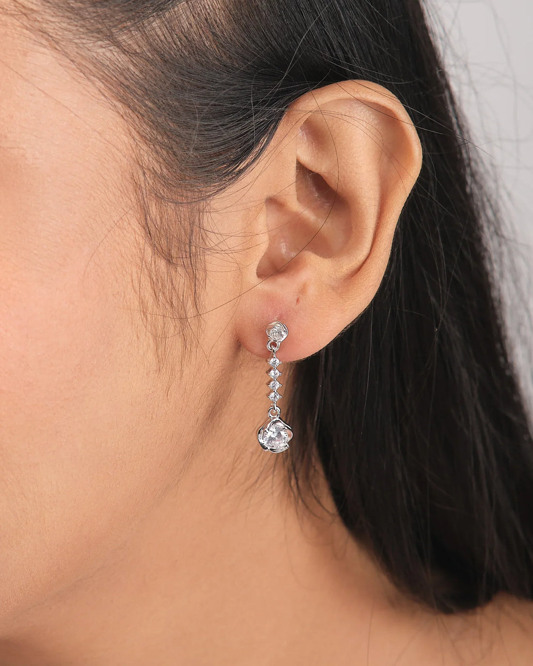 The Barely Bling Silver Earrings by Chandrani Pearls feature round and teardrop-shaped clear CZ stones for easy-care luxury, shown on a white cube with a purple ribbon beside them.