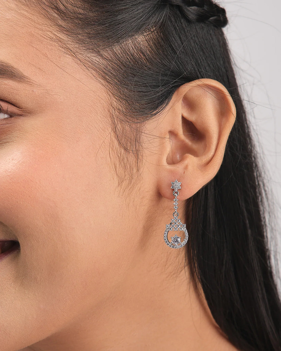 The Slow Sunday Shine Silver Earring by Chandrani Pearls features dainty silver star studs, hanging circles, and sparkling clear gemstones—an elegant accessory for any occasion. Displayed on a white box with a purple ribbon in the background.