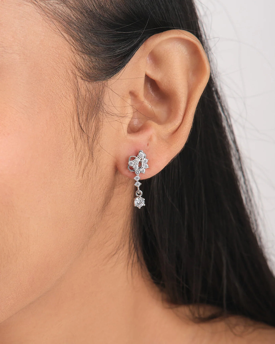 The First Kiss Glow Silver Earrings by Chandrani Pearls, featuring a romantic floral design with small clear CZ stones, are displayed hanging over the edge of a white ceramic bowl with a purple ribbon nearby.