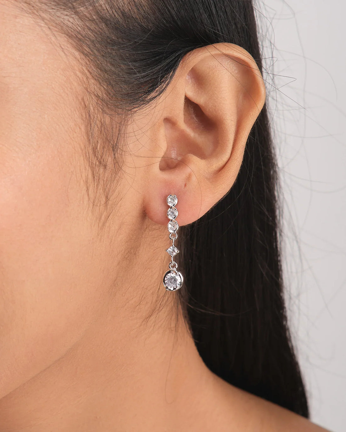 Date Night Lite Silver Earrings by Chandrani Pearls feature multiple round and teardrop-shaped clear gemstones set in silver. Styled against a white bowl with a purple ribbon, they're perfect to add sparkle to your next evening out.