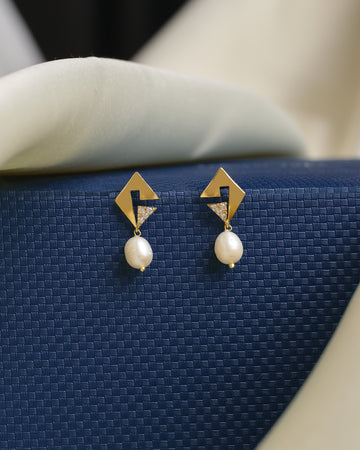 A flawless pearl sits atop a glimmering CZ setting in these Chandrani Pearls earrings, styled on a dark blue textured backdrop with soft fabrics—perfect for adding chic elegance to any look.