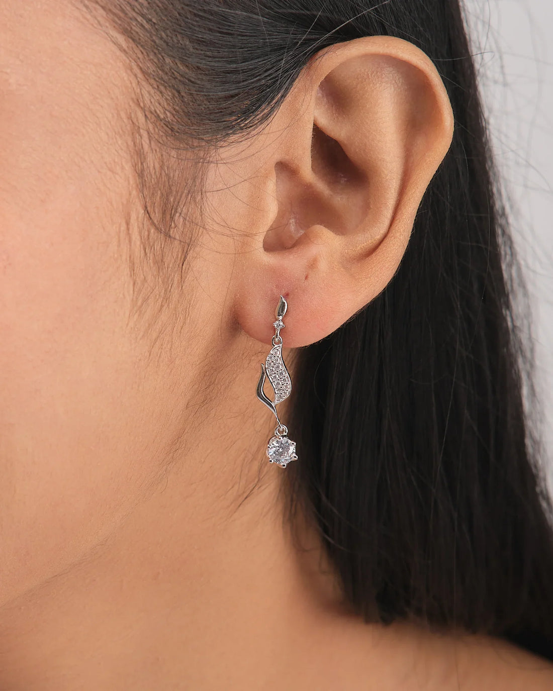 The Statement CZ Earrings in Polished Demifine Silver by Chandrani Pearls hang over a white bowl, sparkling with CZ stones, with a purple ribbon in the foreground.