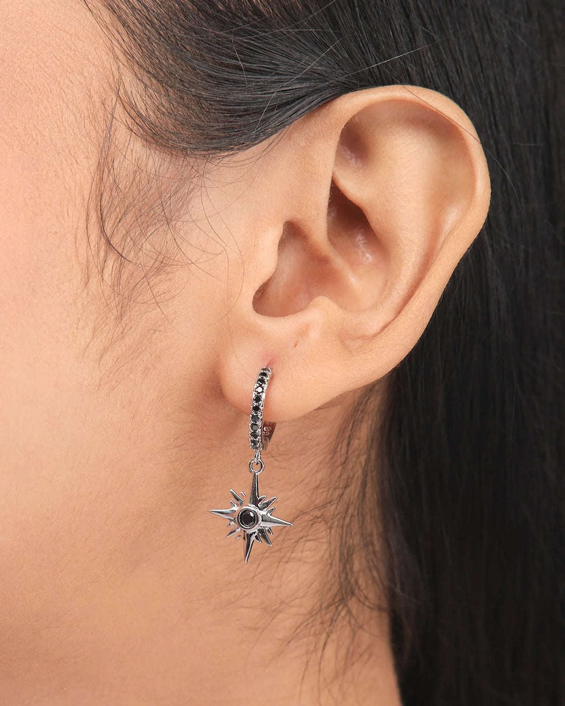 Twinkiling Inspired Demifine Silver CZ Earrings from Chandrani Pearls feature star-shaped dangles with black center stones, shown hanging from a white bowl with a purple ribbon—ideal festive jewelry.