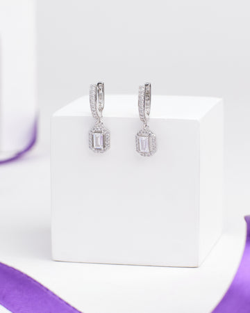 Demifine Silver CZ Earrings Radiant & Refined by Chandrani Pearls—timeless cubic zirconia dangle earrings with rectangular clear stones and round accents, perfect for classic contemporary style. Displayed on a white stand with a purple ribbon.