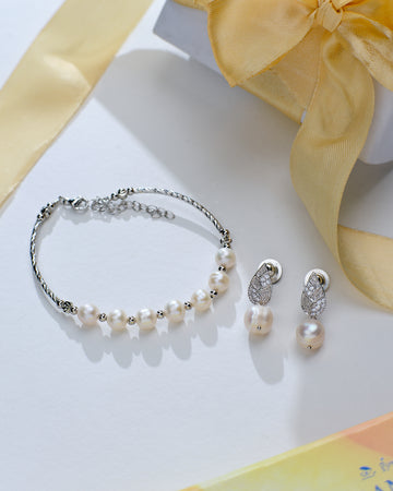 The Pretty Bracelet & Earring Combo Collection by Chandrani Pearls, featuring delicate pearl accents, is displayed next to a jewelry box adorned with a yellow ribbon.