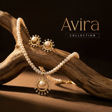 Gold and pearl necklace with matching earrings displayed on a wooden branch, with "Avira Collection" text above.