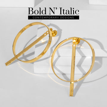 A pair of large, gold circular earrings with geometric bars, displayed on a white surface. Text at the bottom reads "Bold N’ Italic Collection.